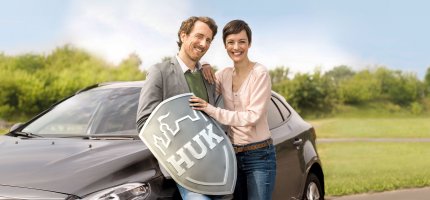 Mann und Frau vor Auto mit HUK-COBURG Schild