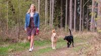 Frau spaziert im Wald mit zwei Hunden.