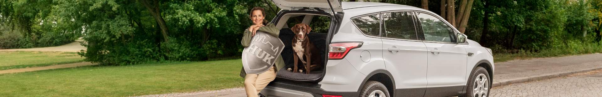 Frau sitzt mit Hund im Auto-Kofferraum 