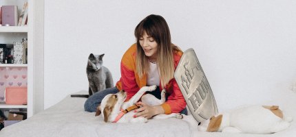 Frau sitzt mit Hund und Katze auf dem Bett