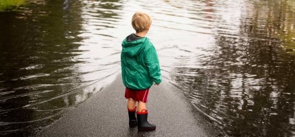 Kleiner Junge steht vor einer überschwemmten Straße