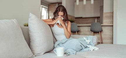 Frau sitzt mit Grippe auf Sofa