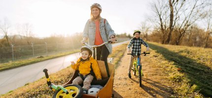 Mama mit Kind im Lastenfahrrad und Sohn auf seinem Fahrrad