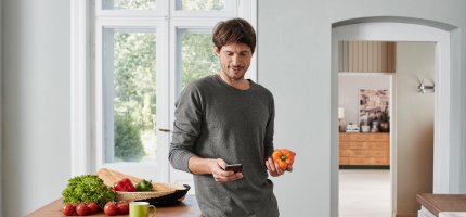 Mann steht in Küche und hält eine Paprika in der Hand