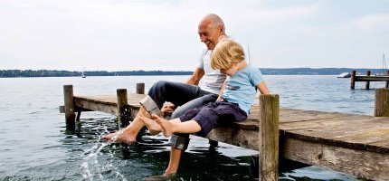 Opa sitzt mit Enkel auf einem Steg am Meer