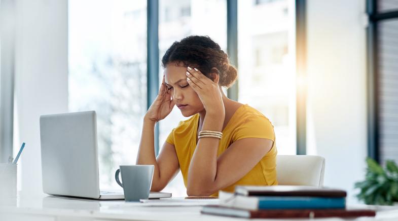 Frau mit Kopfschmerzen hält sich den Kopf am Arbeitsplatz