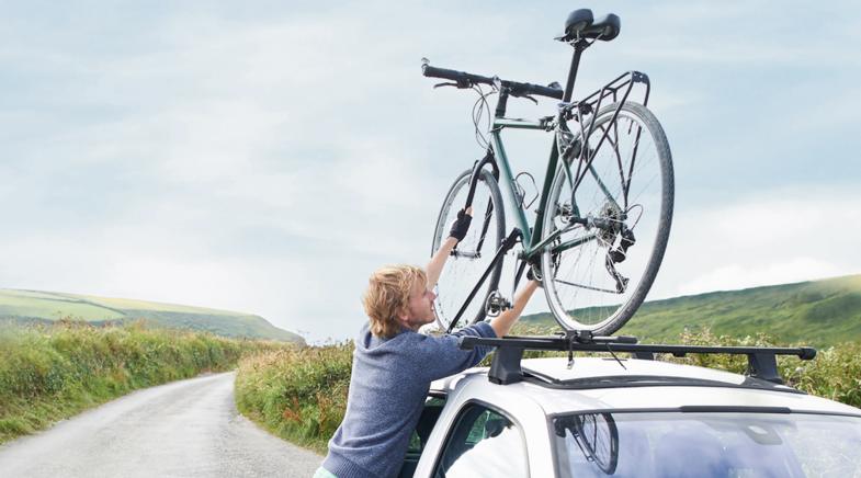 Person befestigt Fahrrad auf dem Autodach