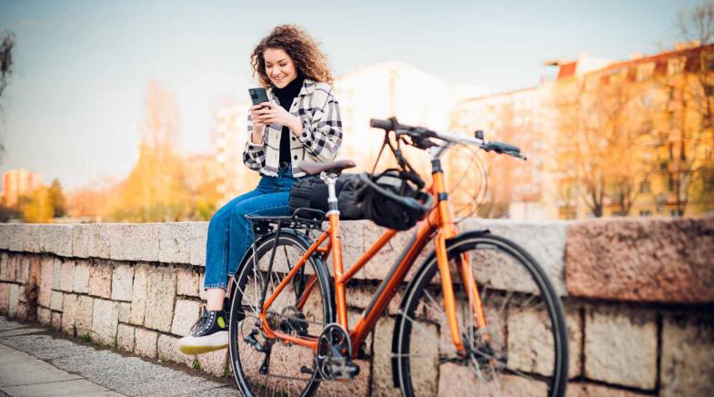 Frau sitzt auf Mauer, neben ihr lehnt ein Fahrrad
