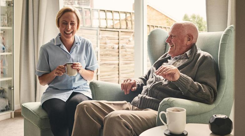 Renter und mittelalte Frau trinken lachend Kaffee und sitzen am Fenster