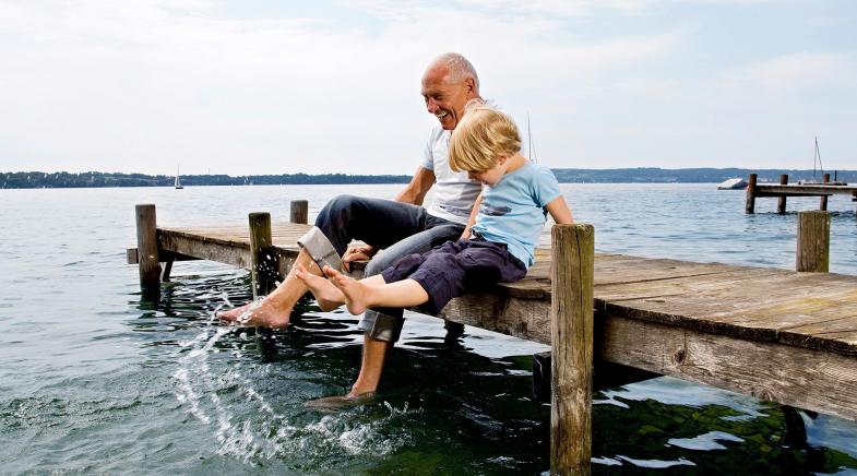 Opa sitzt mit seinem Enkel am See und halten die Füße ins Wasser 