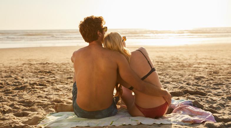 Eine junge Frau und ein junger Mann sitzen am Strand.