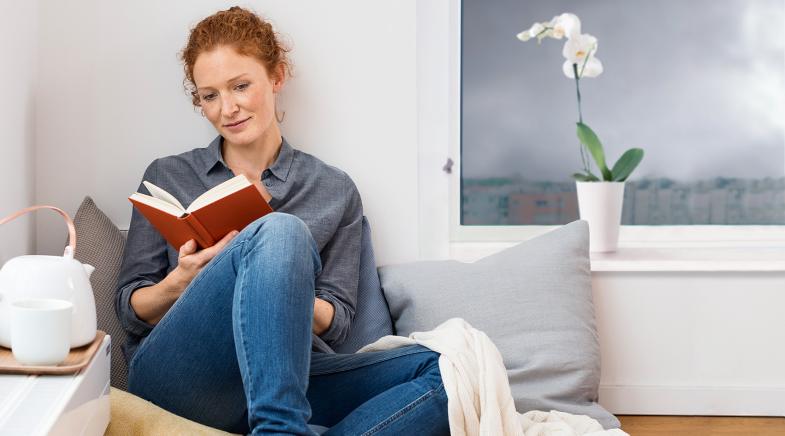 Junge Frau sitzzt vor dem Fenster und liest ein Buch – draußen stürmt es 