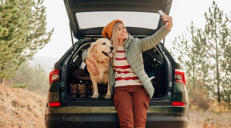 Frau sitzt mit einem Hund im Kofferraum eines Autos