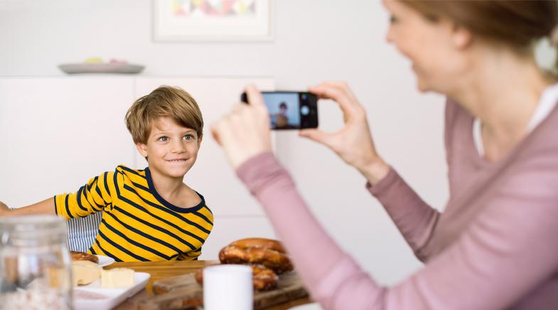 Mutter fotografiert ihren Sohn am Tisch.