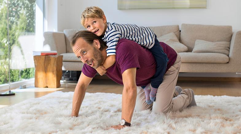 Vater kniet auf dem Teppich mit Sohn auf dem Rücken