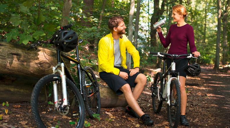 Mann und Frau machen eine Trinkpause vom Fahrradfahren im Wald