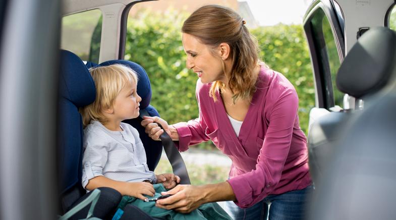 Mutter schnallt ihr Kind im Kindersitz auf der Rücksitzbank des Autos an