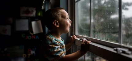 Kleiner Junge steht am Fenster und beobachtet den Regen