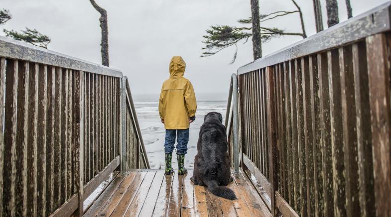 Kleiner Junge und Hund stehen bei Regen auf einer Brücke und beobachten das Meer